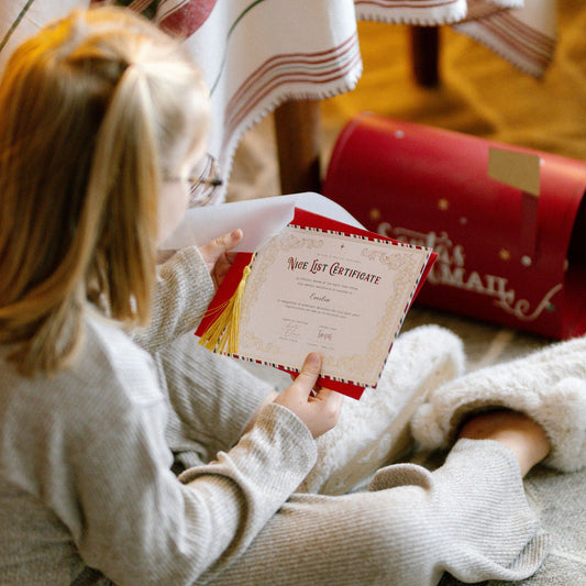 Child sitting on a carpeted floor holding a letter, with a striped blanket and wrapped gift in the background.