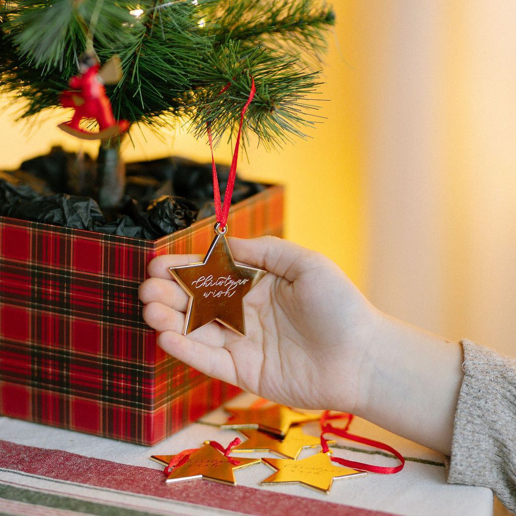 Hand holding a Christmas tree ornament that reads Christmas Wish, in front of a decorated tree